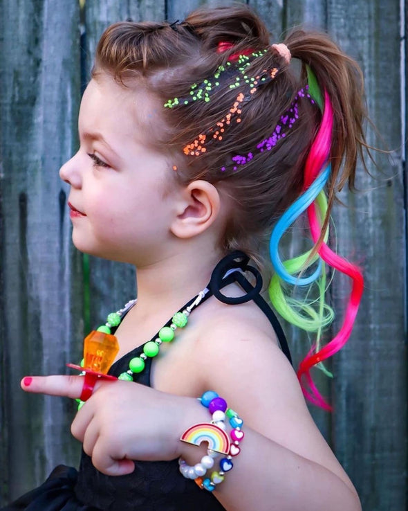 Little girl in clip in hair extensions in neon pink, blue and yellow green. 